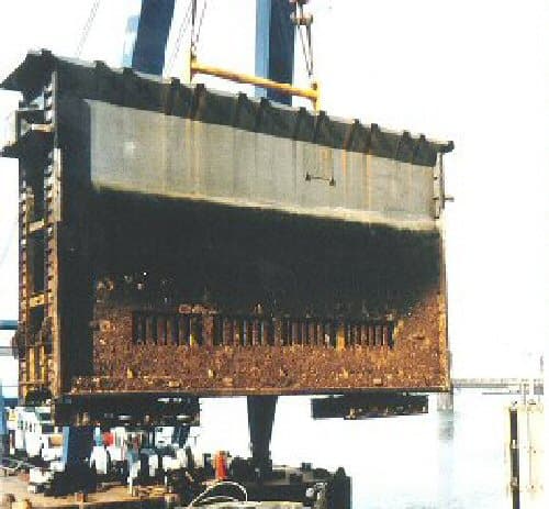 A large waterway lock gate being hoisted by crane, showing the journal-bearing pintle at its base